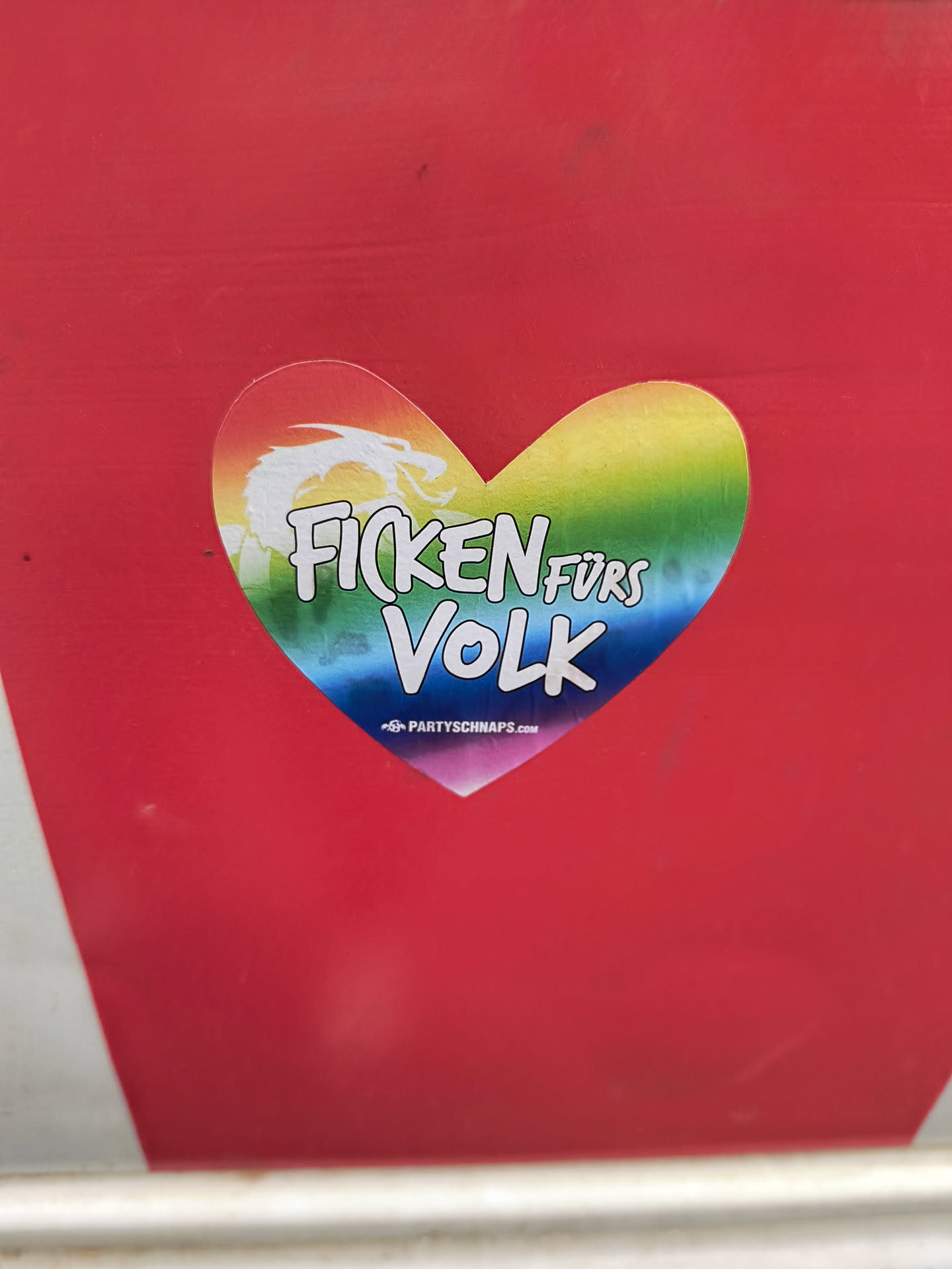 Heart-shaped sticker with a rainbow design, a dragon, and the text "Ficken fürs Volk."  The text is written in German and translates roughly to "Fuck for the People". A website address is also visible at the bottom.