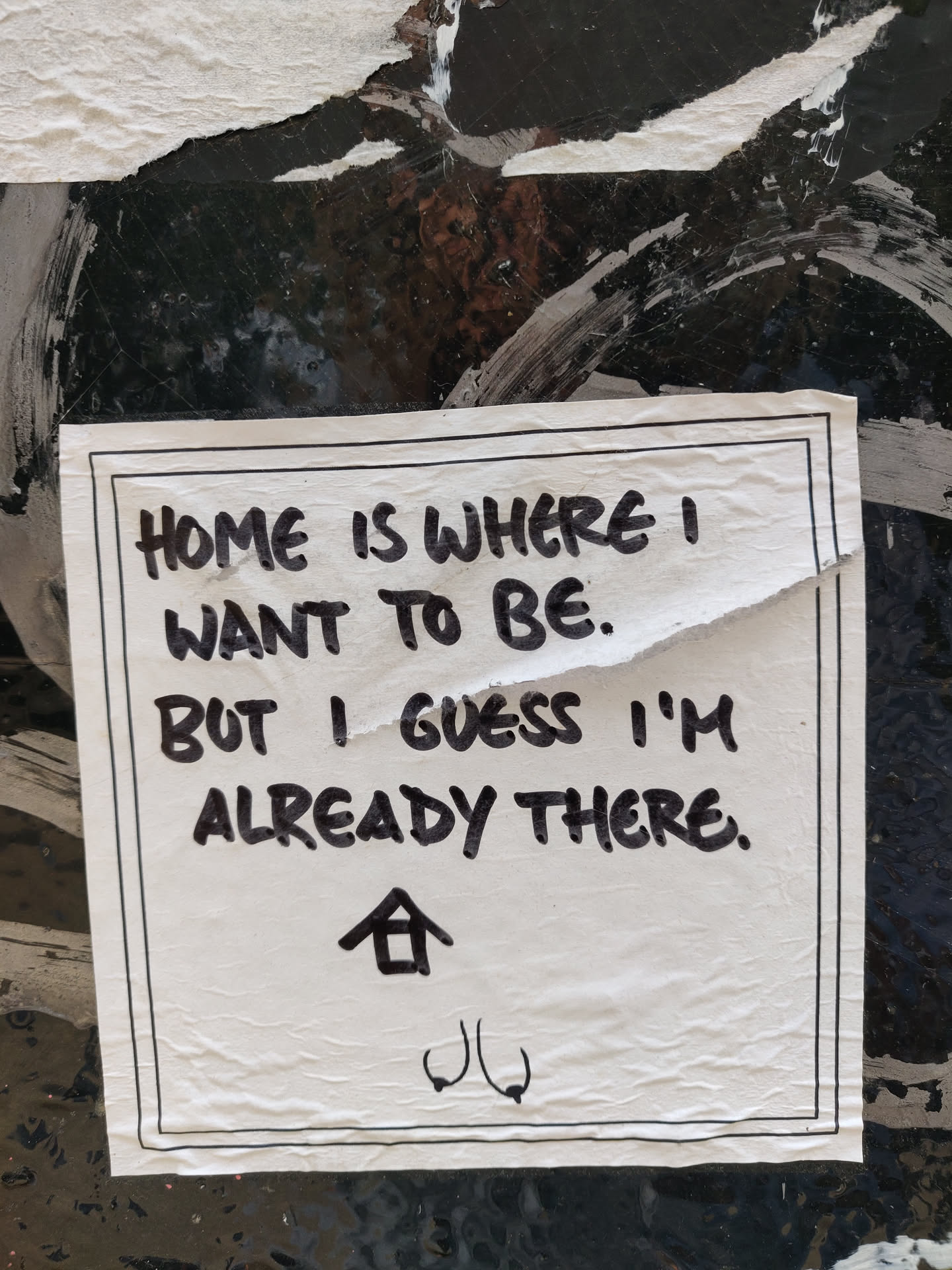 A minimalist sticker with a handwritten quote. The sticker has a black border and features a small house symbol and a unique symbol at the bottom.
