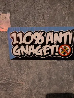 Street sticker A rectangular street sticker featuring bold, distressed white lettering with thick black outlines that reads '110% ANTI GNAGET!'. The background features light blue and dark blue sections. On the lower right, the crest of AIK (Allmänna Idrottsklubben) is displayed inside a red prohibition circle with a diagonal red line crossing it out.