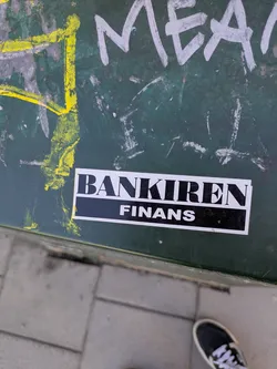 A sticker for "Bankiren Finans" is seen affixed to a green surface. The sticker has a black background with white text.