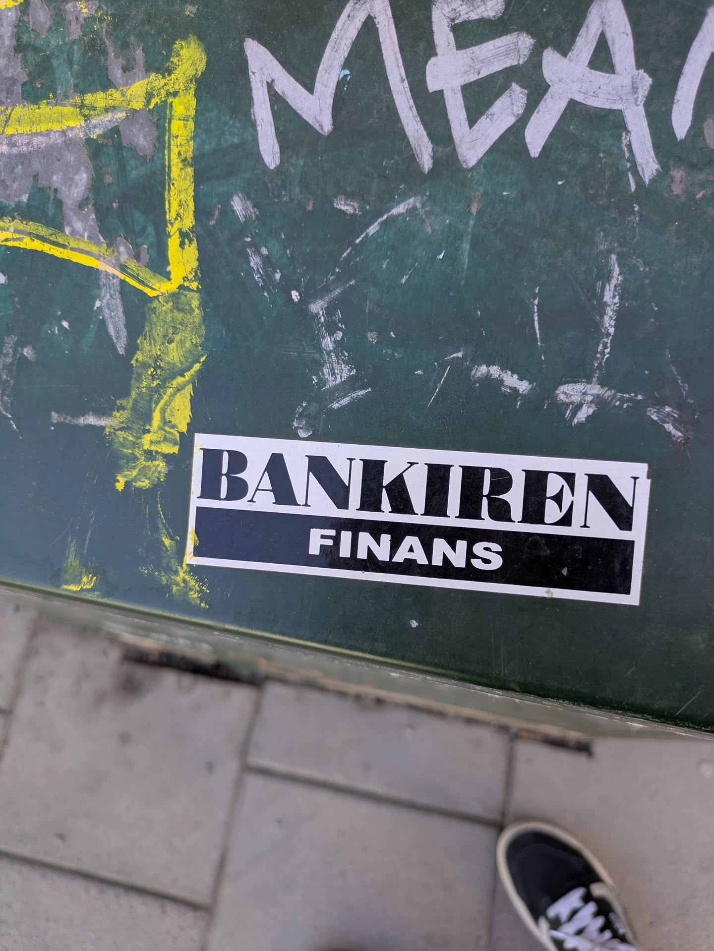 A sticker for "Bankiren Finans" is seen affixed to a green surface. The sticker has a black background with white text.