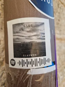 A black and white photo of a beach with structures in the background.  The Spotify code is present at the bottom of the sticker. 