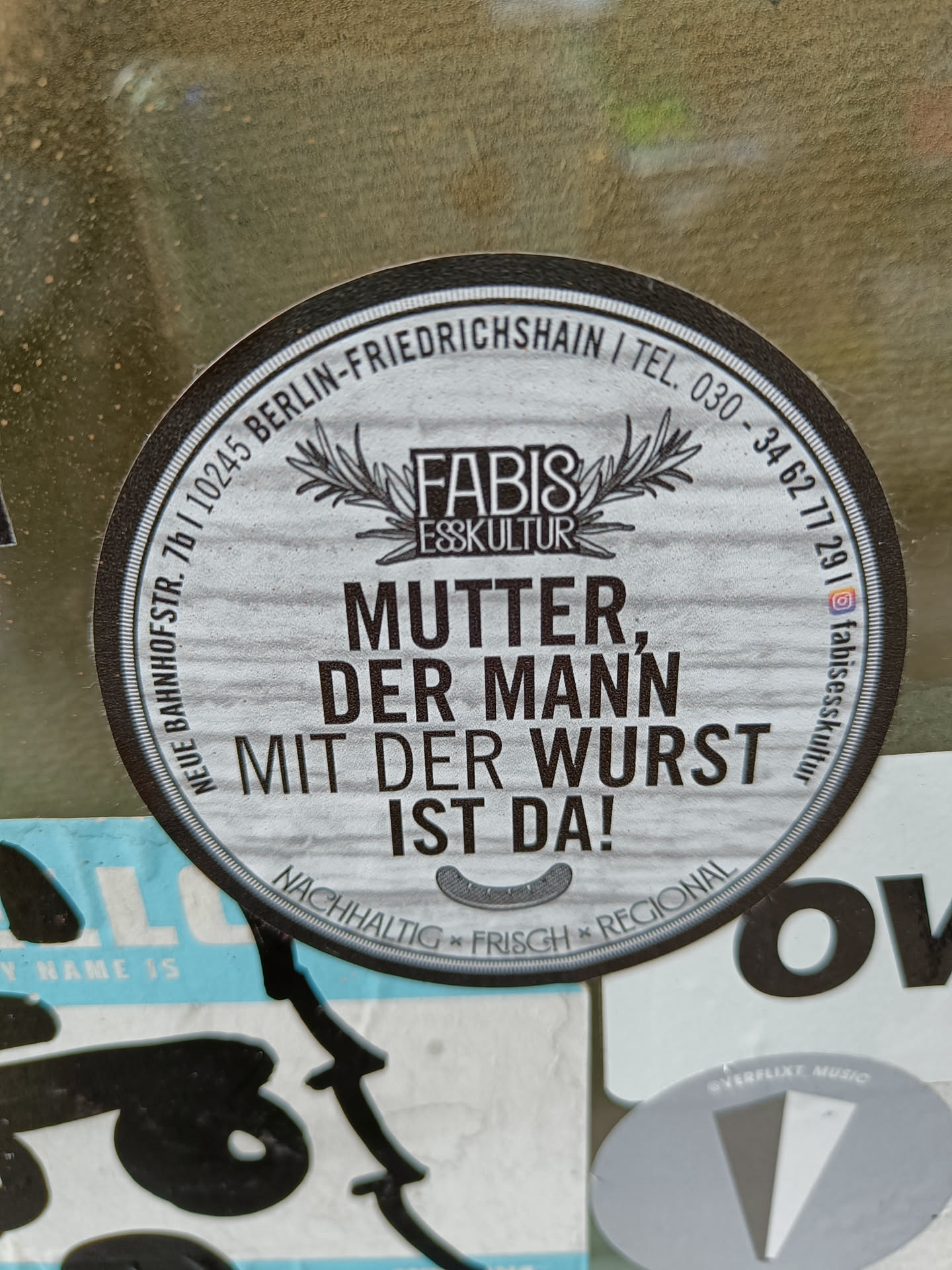 Round sticker with the text "Mutter, der Mann mit der Wurst ist da!" (Mother, the man with the sausage is here!),  Fabis Esskultur logo and contact info. It mentions sustainability, freshness and regionality.