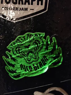 A neon green sticker featuring a snarling tiger head surrounded by stylized flames.  The artist's name, "Nico Braun," is prominently displayed, along with their Instagram handle.