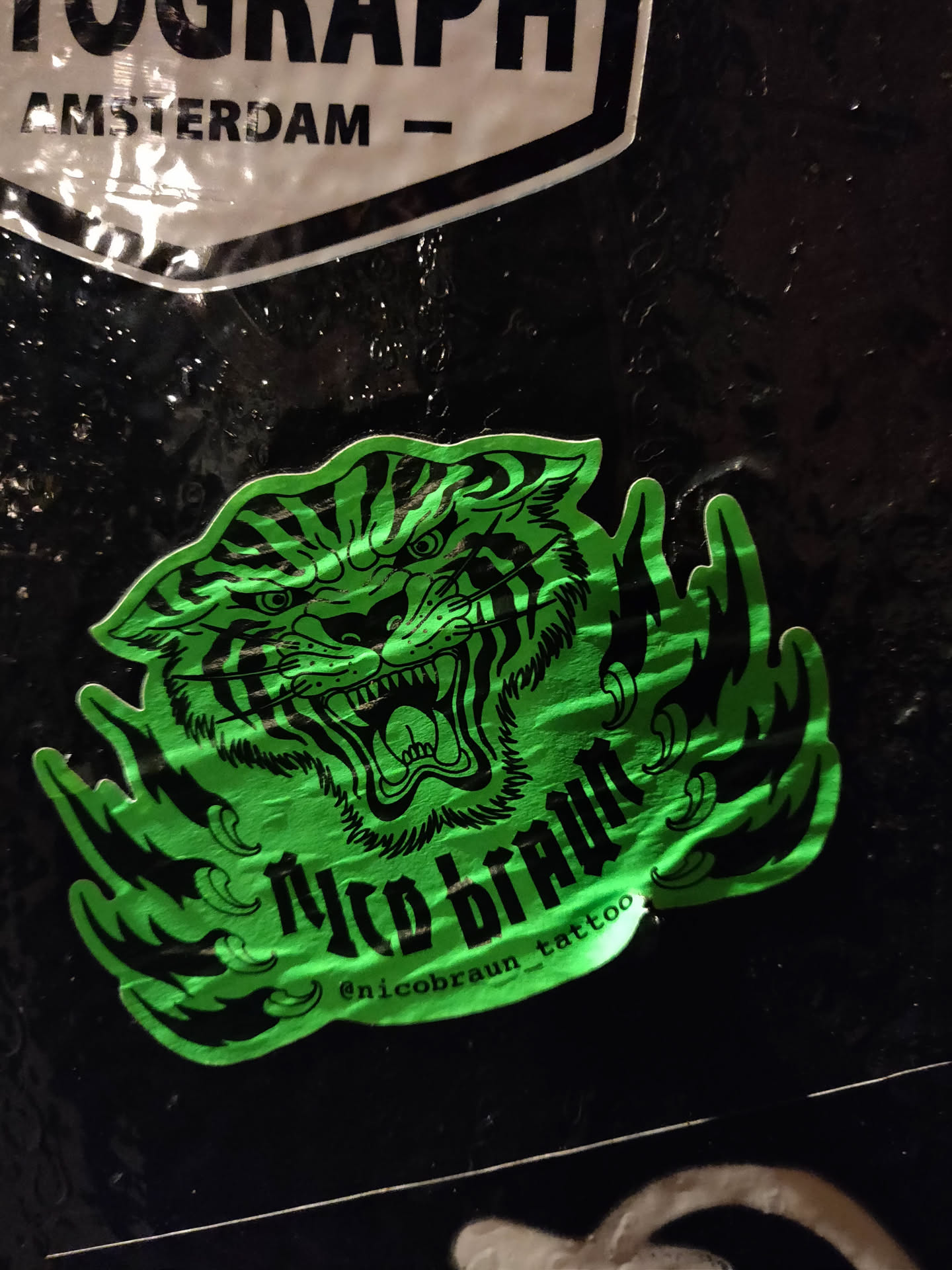 A neon green sticker featuring a snarling tiger head surrounded by stylized flames.  The artist's name, "Nico Braun," is prominently displayed, along with their Instagram handle.
