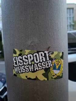 A sticker featuring the logo of EisSport Weisswasser, a German ice hockey club. The sticker has a camouflage background with the team's name prominently displayed. A crest of the city is included. 