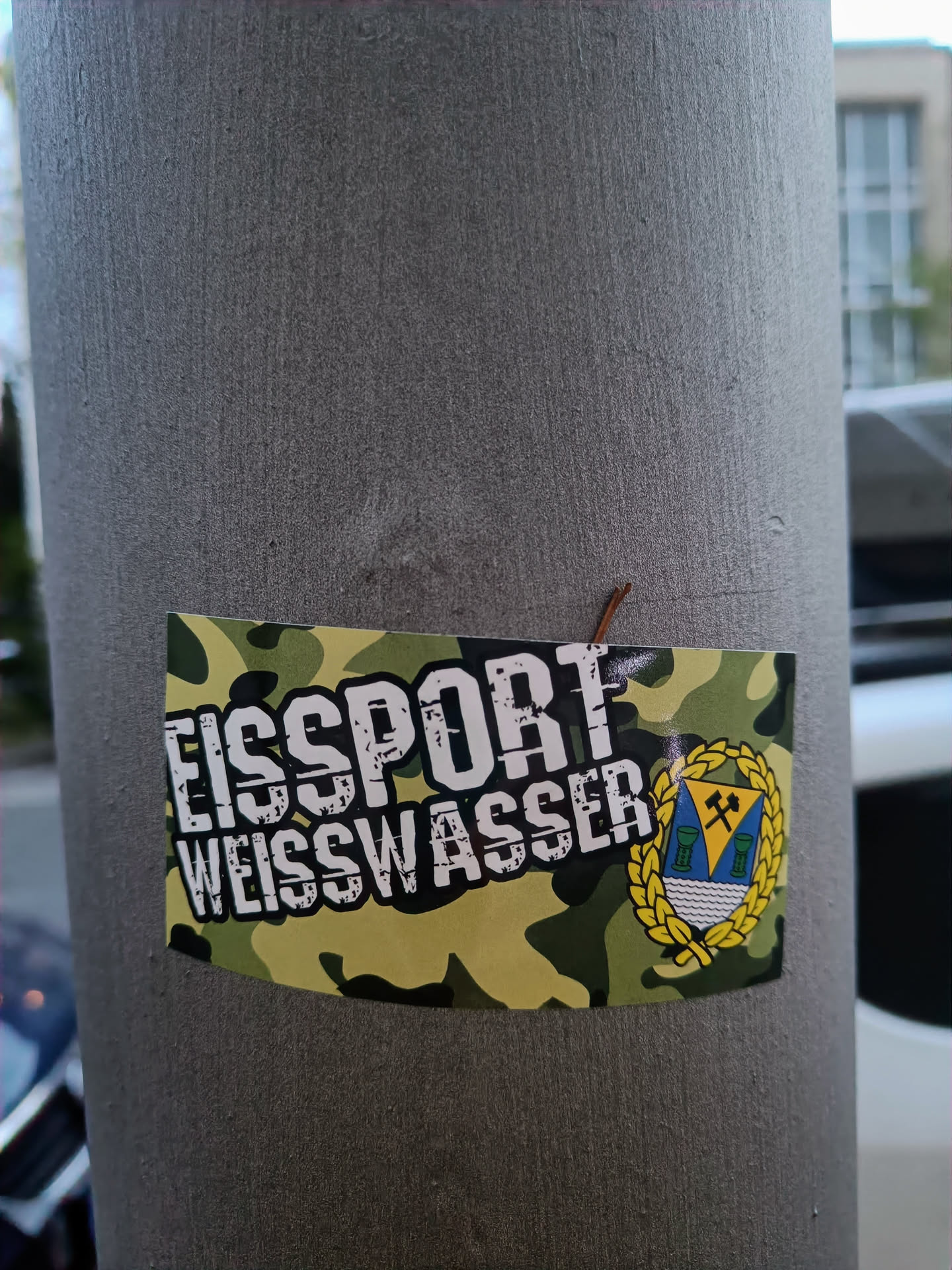 A sticker featuring the logo of EisSport Weisswasser, a German ice hockey club. The sticker has a camouflage background with the team's name prominently displayed. A crest of the city is included. 