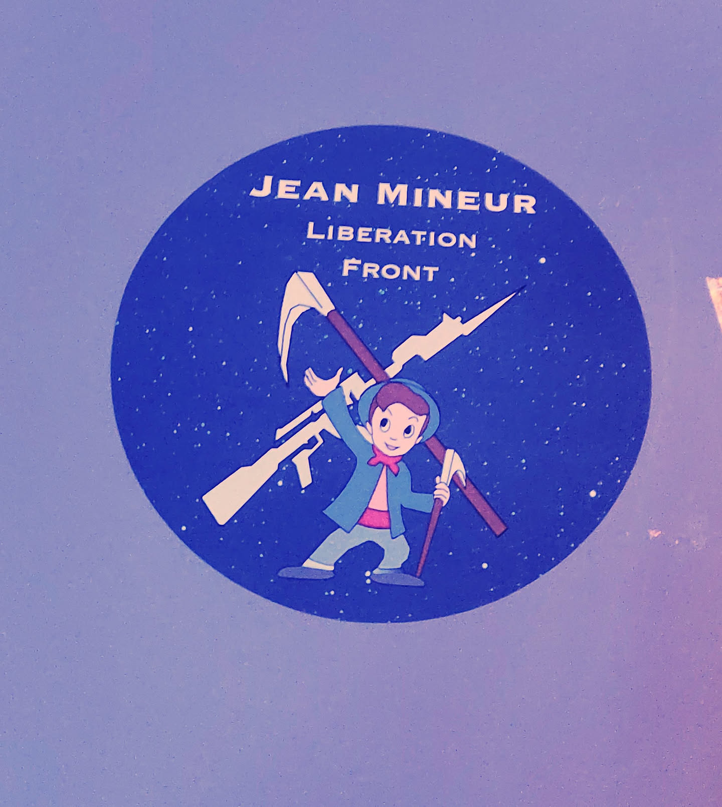 A round sticker featuring a cartoon illustration of a boy carrying weapons, with the text "JEAN MINEUR LIBERATION FRONT" above.