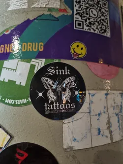 Black and white sticker with a butterfly and the text 'Sink tattoos' and Instagram handle @silvainpocciati.