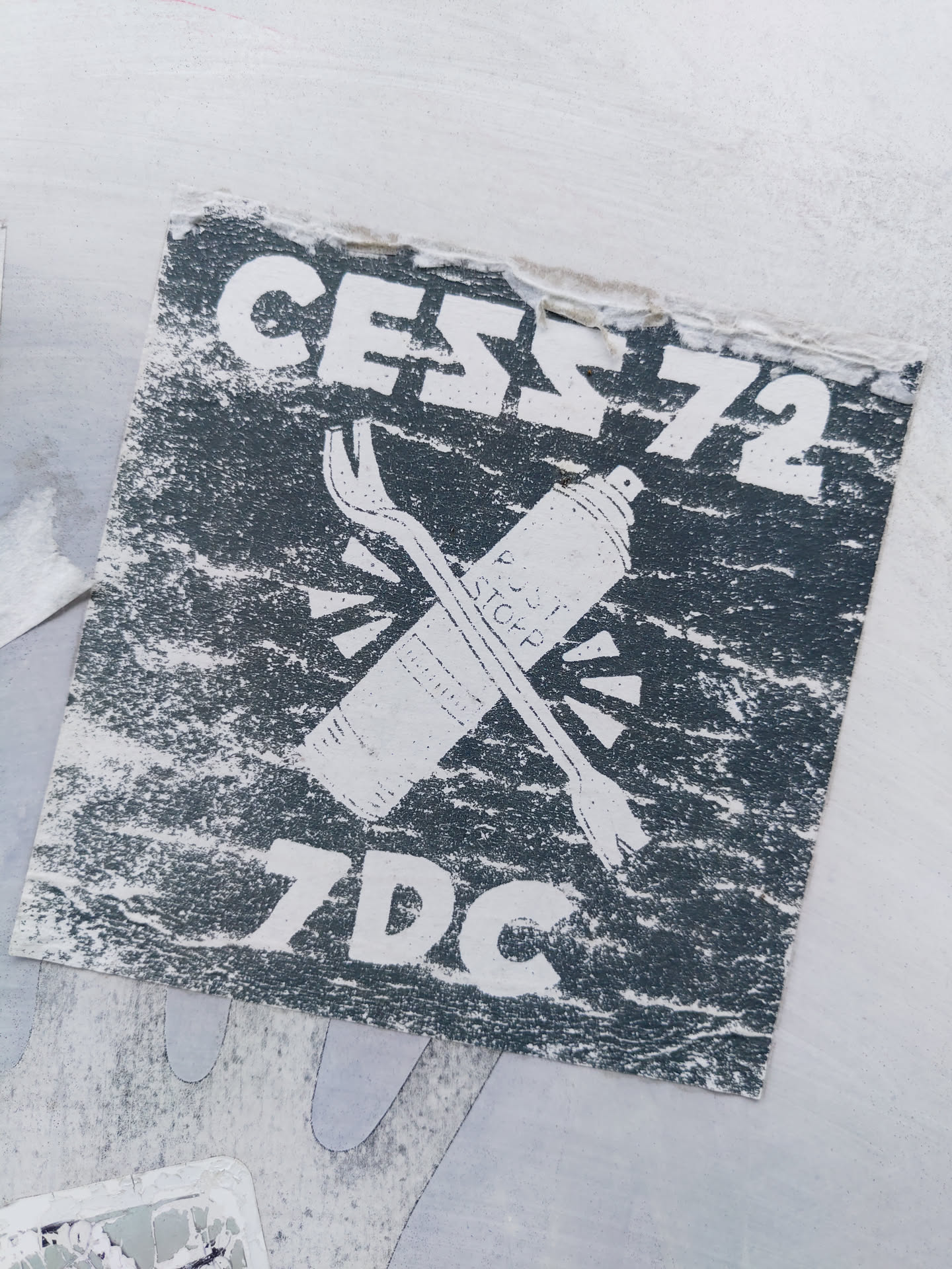 A dark grey sticker featuring the text "CESS72" at the top and "7DC" at the bottom.  A graphic of a spray can and a crowbar are crossed in the center. The style is reminiscent of graffiti art.