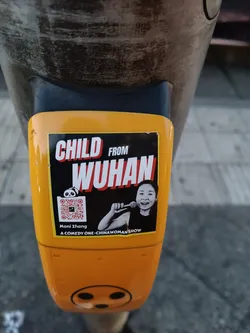 A yellow sticker featuring Moni Zhang, a stand-up comedian, promoting her comedy show. The sticker includes a QR code and text that says "Child from Wuhan" and "A comedy one-Chinawoman show."