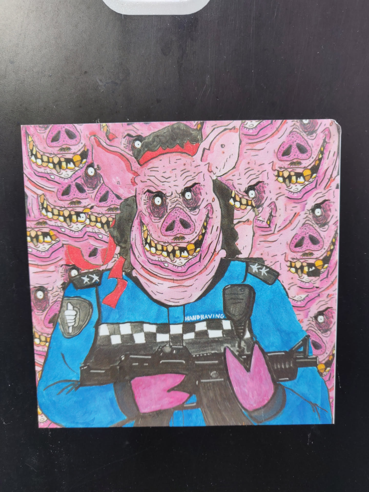 A sticker depicting a pig dressed as a police officer, holding a rifle. The pig is surrounded by a multitude of other pig heads, all with similar grotesque features. The art style is cartoonish and slightly disturbing. The pig's uniform includes a police hat and a checkered pattern on the chest. The background is a repeating pattern of pig heads.