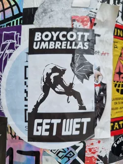 A black and white sticker featuring a stylized figure rejecting an umbrella with the text "Boycott Umbrellas" and "Get Wet".