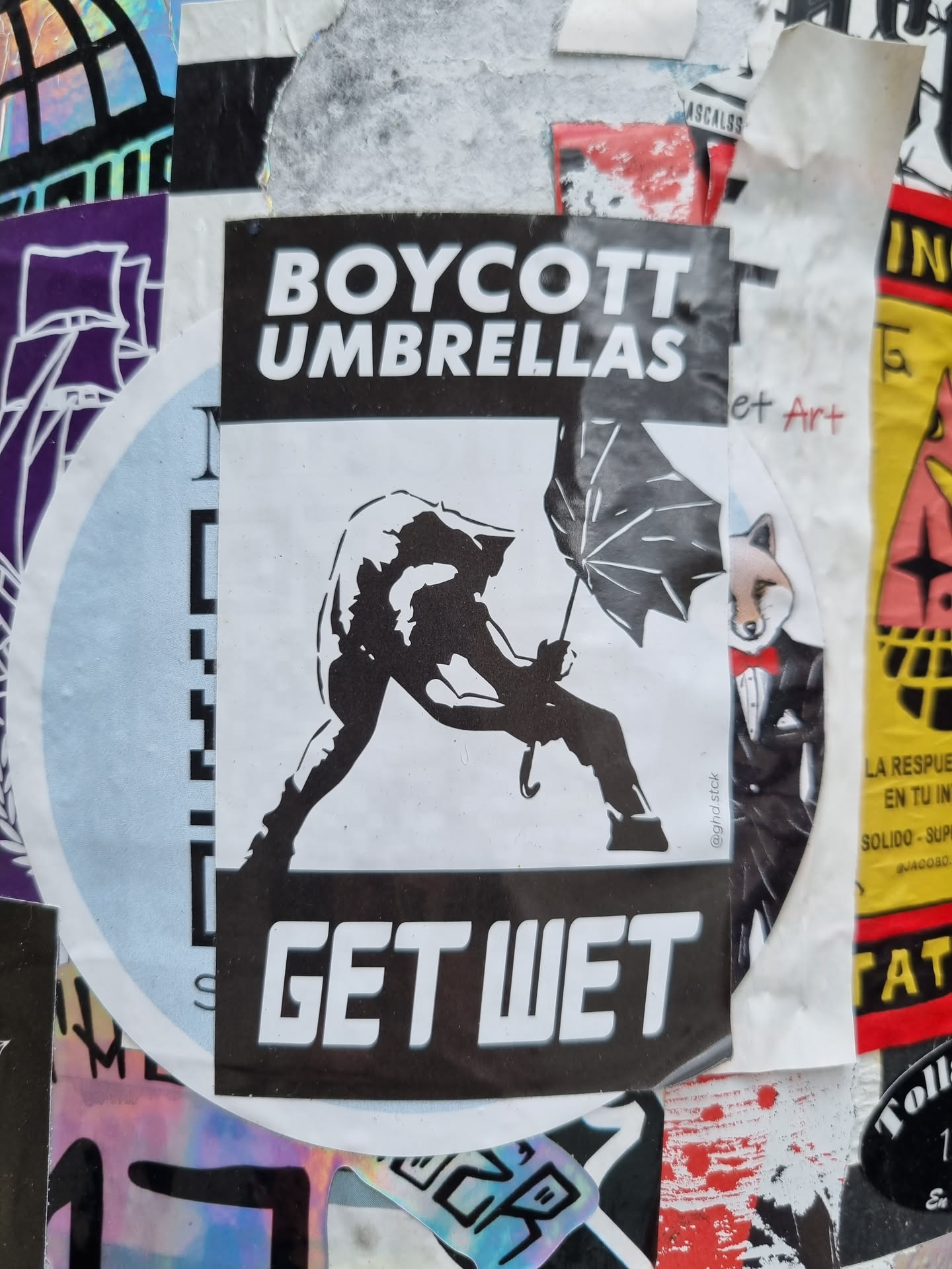 A black and white sticker featuring a stylized figure rejecting an umbrella with the text "Boycott Umbrellas" and "Get Wet".