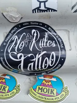 A black and white circular sticker with the text "No Rules Tattoo" in a stylized script font.  It also includes the address "viale fiume 16, Marina di Ginosa (TA)", an email address danilomilfatattoo@icloud.com and a phone number 346.3170625. A small tattoo machine is depicted within the circle.