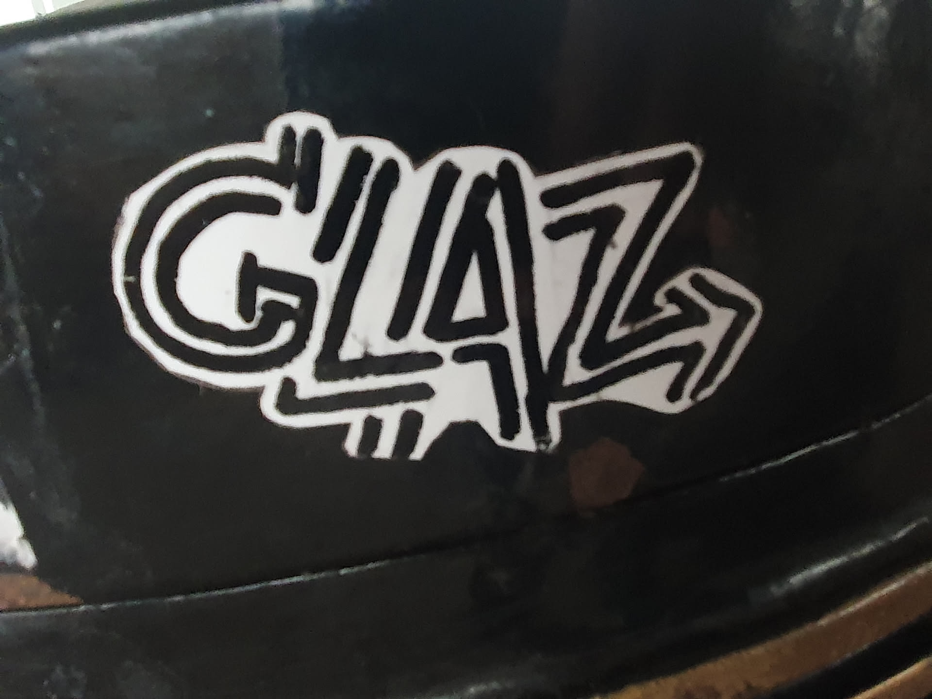 Black and white sticker with the word GLAZ stylized in a graffiti-like font. The sticker has a slightly worn look, suggesting it may have been placed outdoors. 