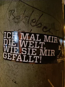 A black sticker with white German text that says: I paint the world as I like it. There is a logo on the right side of the sticker. 