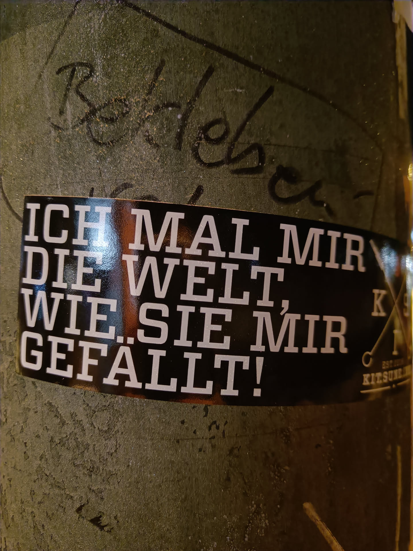 A black sticker with white German text that says: I paint the world as I like it. There is a logo on the right side of the sticker. 