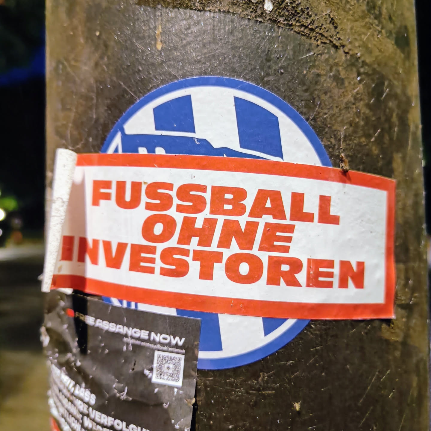 A sticker expressing the sentiment of football without investors.  It features bold red and white text on a rectangular sticker layered over a circular blue sticker with a partially visible design that might be football-related. The main text is in German.