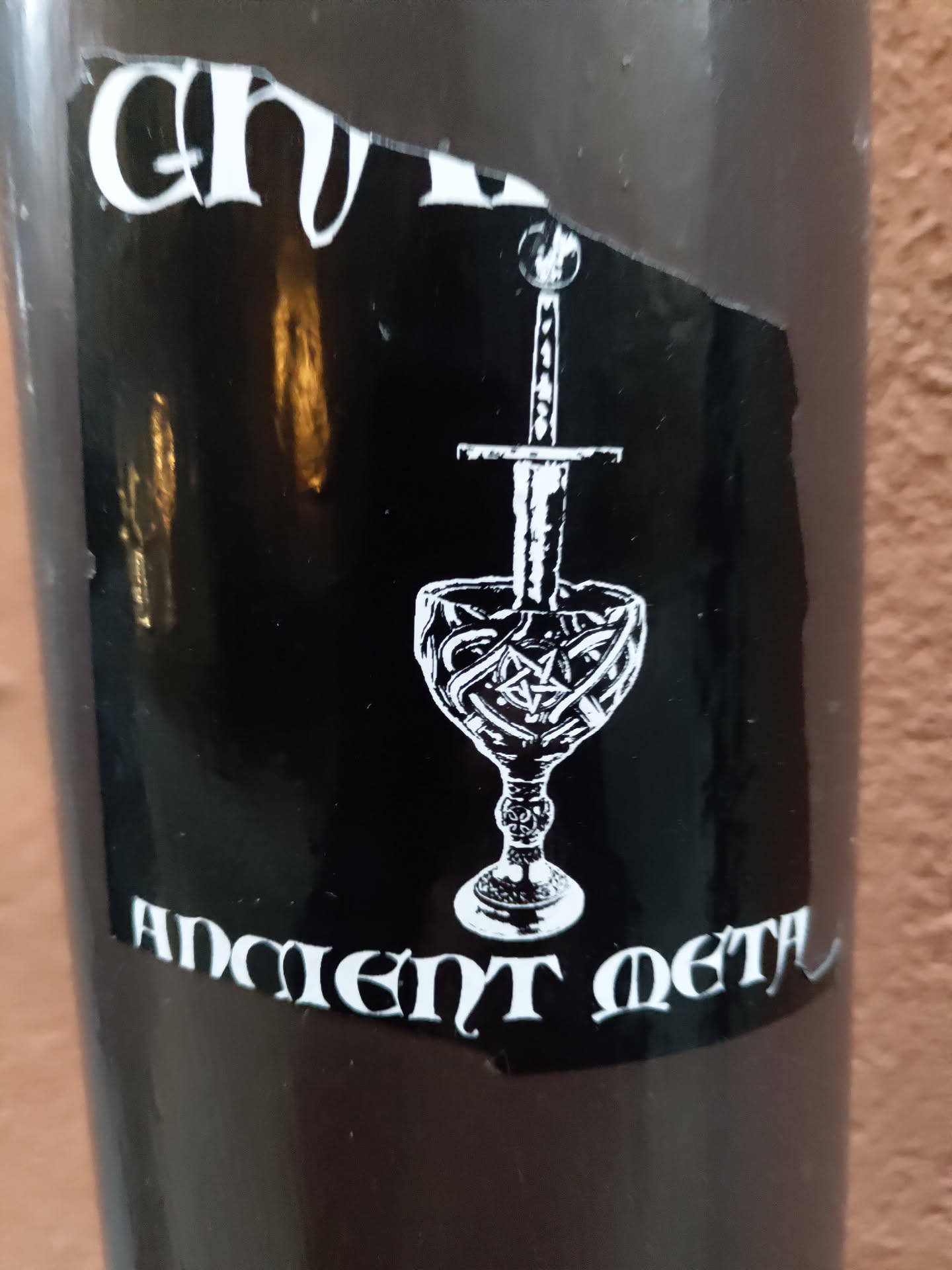 Black and white sticker with a goblet and a sword. The text "Ancient Metal" is visible at the bottom. 