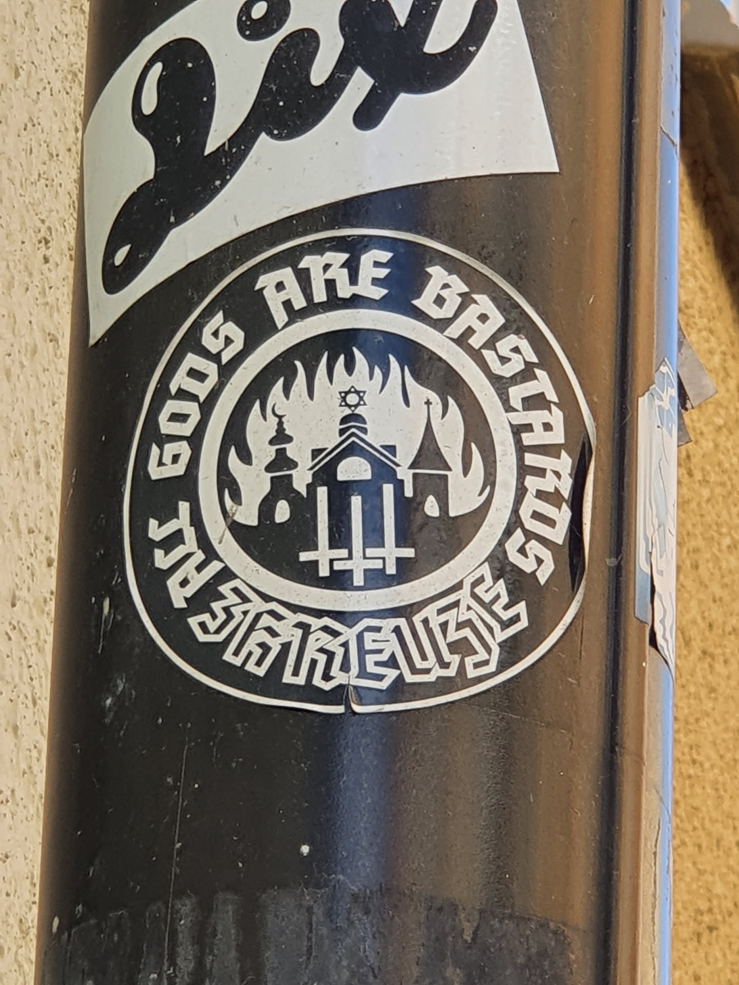 Black and white circular sticker with a design depicting a burning building with religious symbols, surrounded by text that says "Gods Are Bastards".