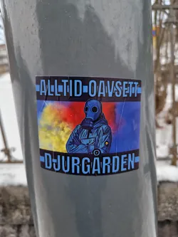 A sticker featuring a person in a gas mask, with the text "Alltid oavsett" above and "Djurgården" below the image. The background features a colorful smoke effect.