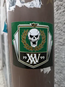 A sticker featuring a skull emblem with a laurel wreath, the roman numerals XV, and the years 19 and 99. It appears to commemorate a 25th anniversary.