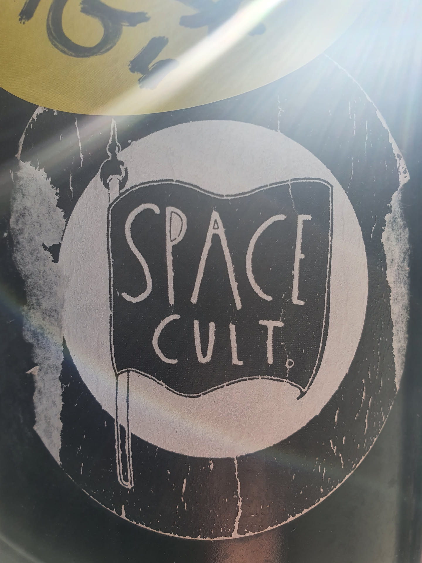 A black and white sticker with a flag design. The flag has the words "SPACE CULT" written on it. The sticker is slightly worn around the edges.