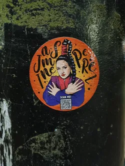 Street sticker Round sticker featuring a stylized illustration of a woman with a high ponytail, resembling a Spice Girl. The woman is depicted in a purple top, with text surrounding her that reads 'I'm the Spice'. A QR code is present at the bottom, labeled 'Scan Me'. The sticker has an orange background and is placed on a dark surface.