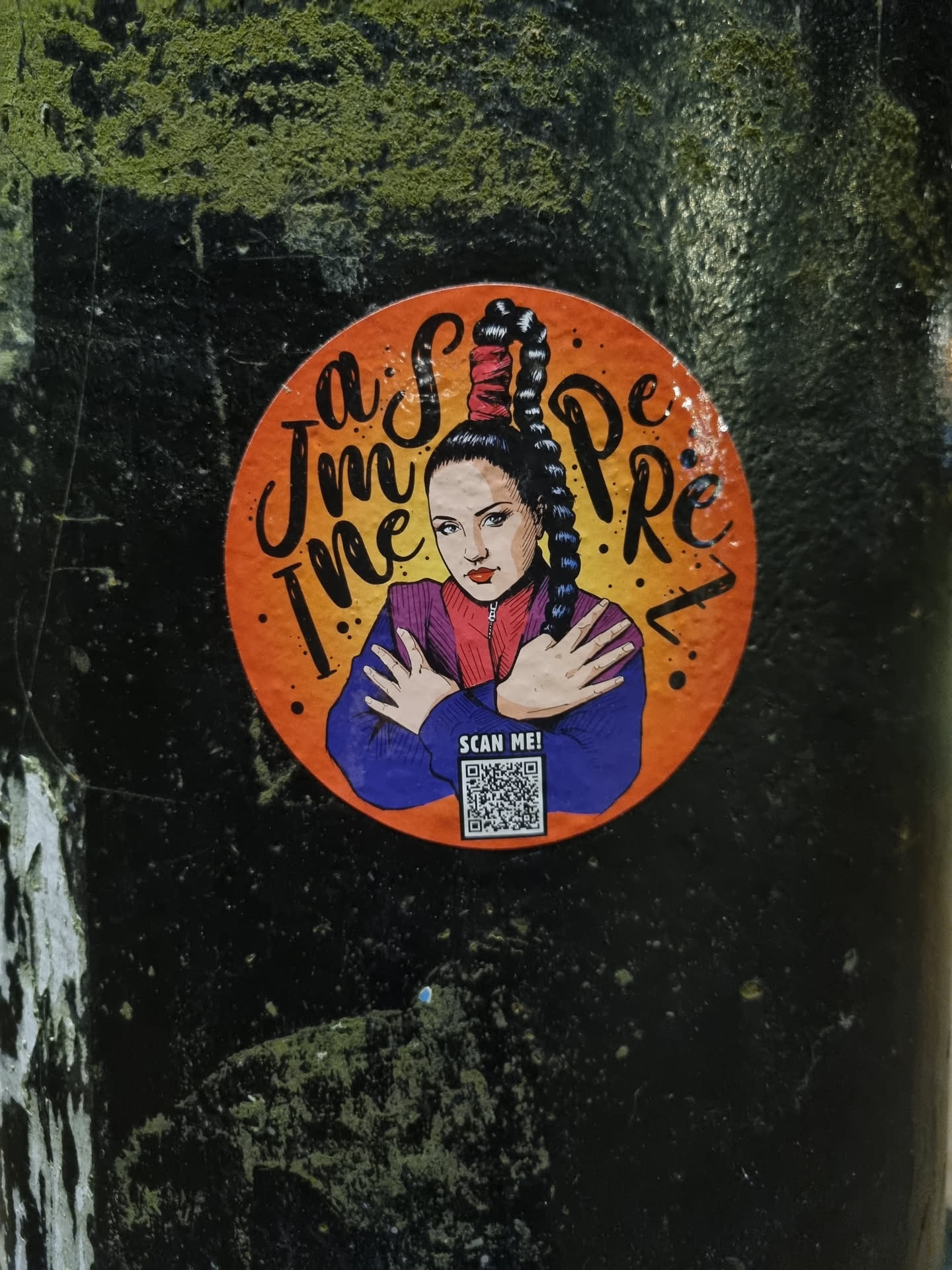 Round sticker featuring a stylized illustration of a woman with a high ponytail, resembling a Spice Girl. The woman is depicted in a purple top, with text surrounding her that reads 'I'm the Spice'. A QR code is present at the bottom, labeled 'Scan Me'. The sticker has an orange background and is placed on a dark surface.