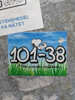 A sticker featuring Snoopy and Woodstock from the Peanuts comic strip. The number 101-38 is prominently displayed in the center. The artwork is set against a backdrop of a blue sky and green grass. 