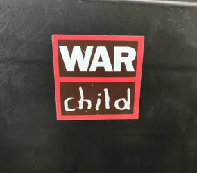 A sticker with the words "WAR" in bold capital letters on top and "child" written in a child-like scrawl underneath. The sticker has a red border and a dark brown background.