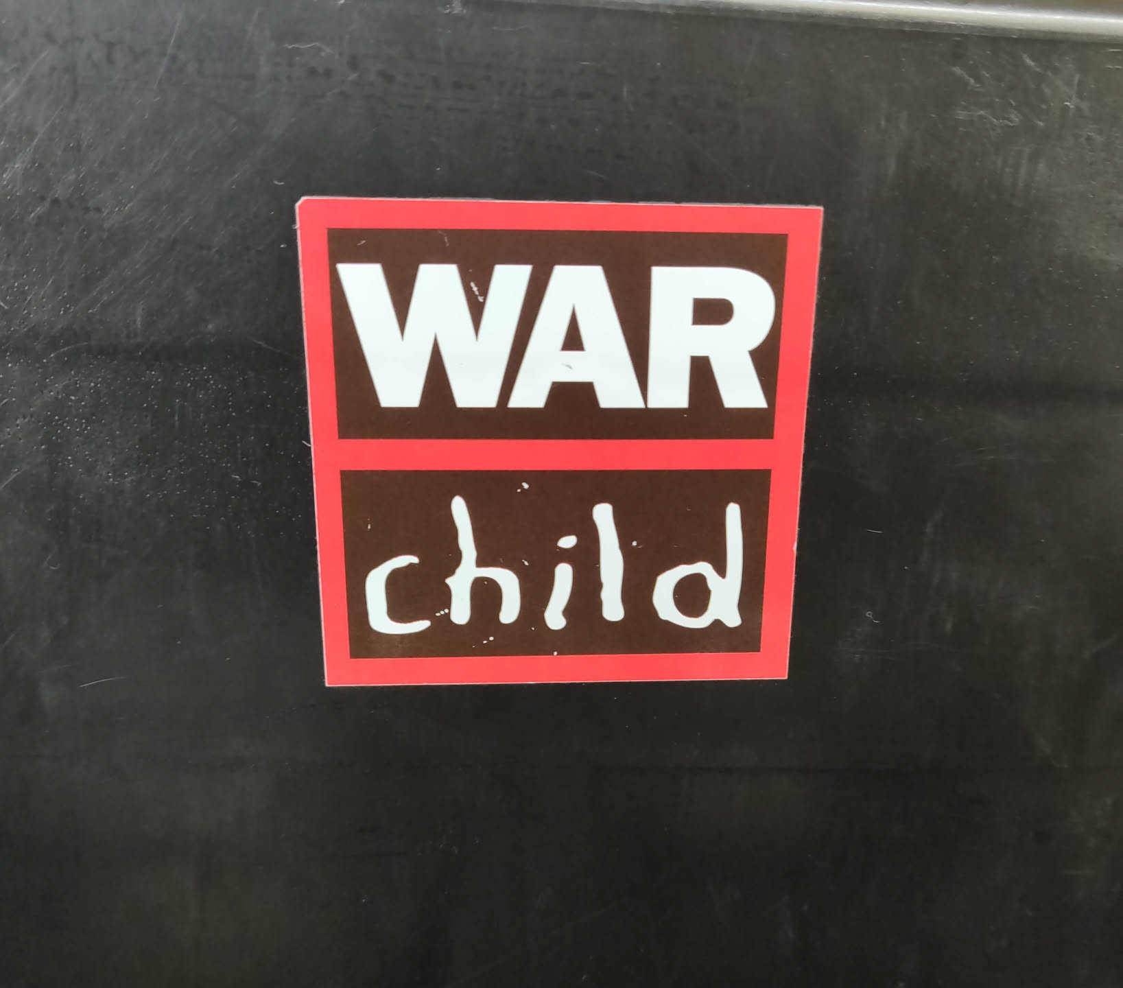A sticker with the words "WAR" in bold capital letters on top and "child" written in a child-like scrawl underneath. The sticker has a red border and a dark brown background.