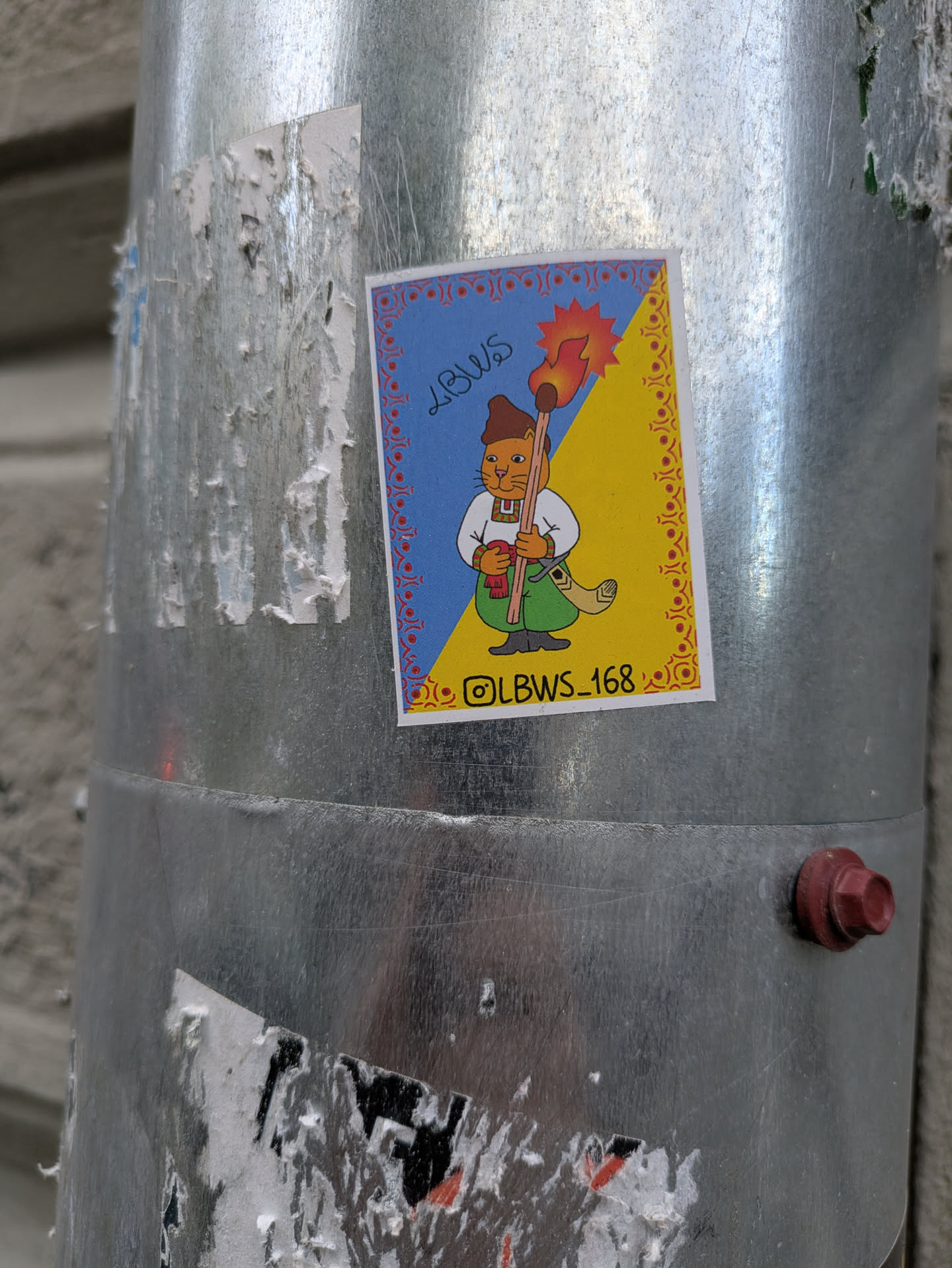 The sticker shows a cartoon cat-like character with a match on a blue and yellow background. The sticker has a border with floral and star-like designs. The text "LBWS" is written at the top left and the Instagram handle "@LBWS_168" is at the bottom.