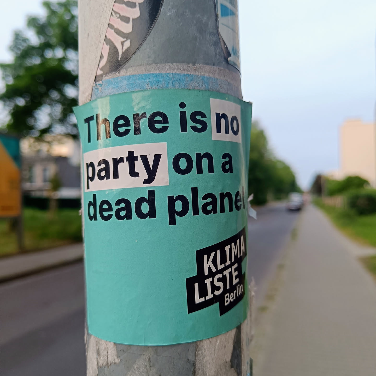 A teal sticker with the text "There is no party on a dead planet" and a logo for Klima Liste Berlin. The sticker is affixed to a pole outdoors.