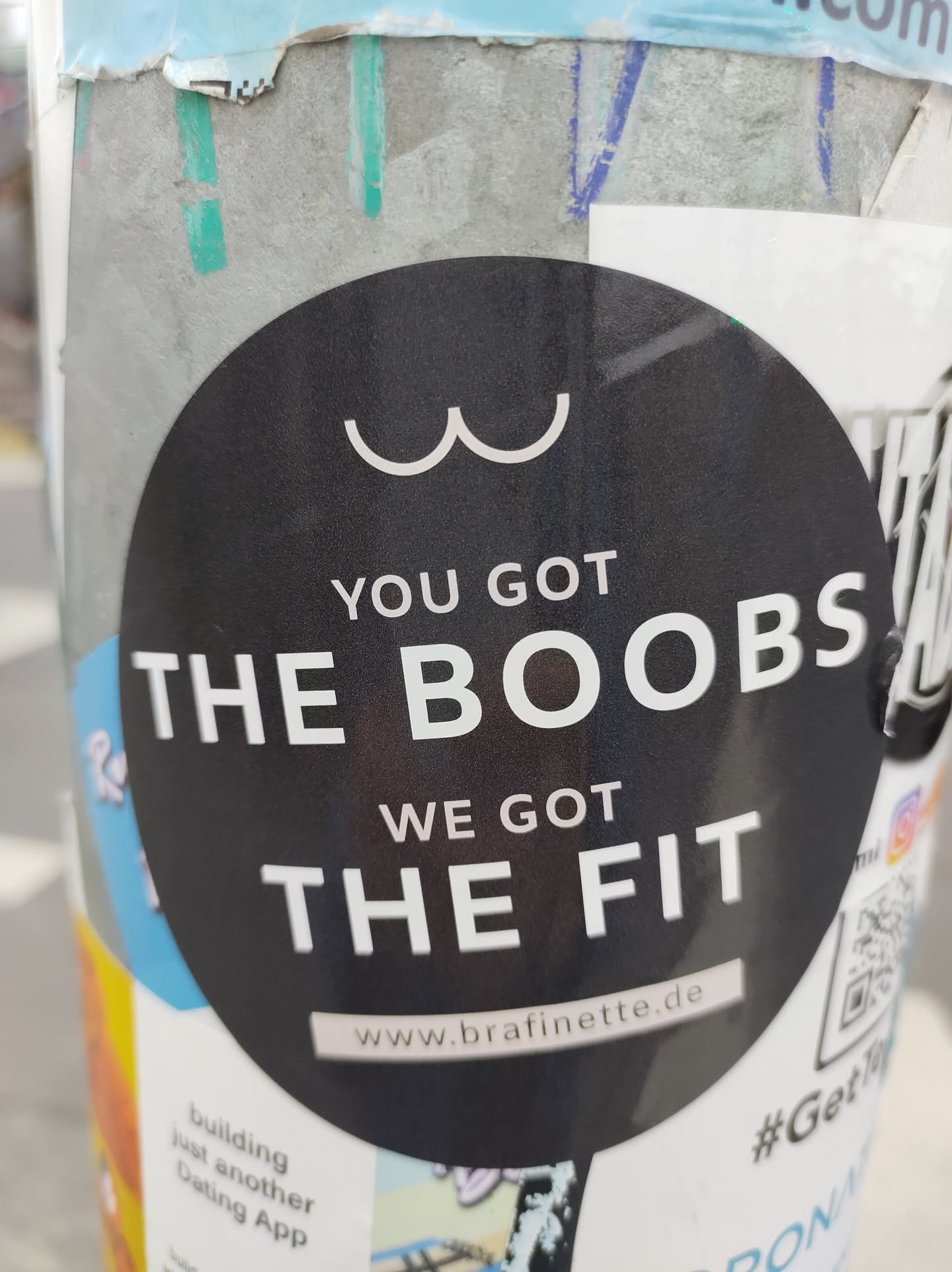 A black round sticker with white text on it. It says "YOU GOT THE BOOBS WE GOT THE FIT" and has a website address at the bottom: www.brafinette.de. There is a minimalist drawing of boobs at the top. 