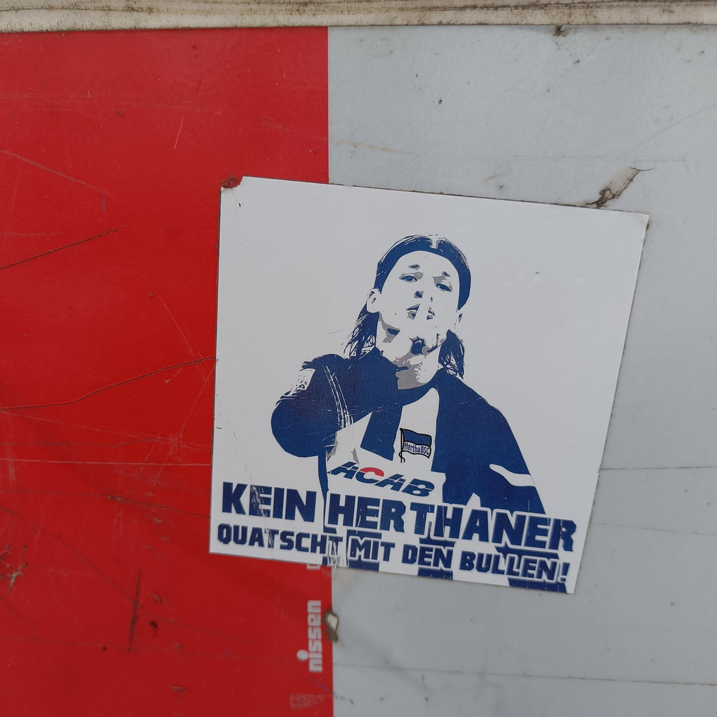 Sticker featuring a stylized image of a person with long hair making a silencing gesture.  Text on the sticker says "Kein Herthaner Quatsch mit den Bullen!" and includes the acronym ACAB. 
