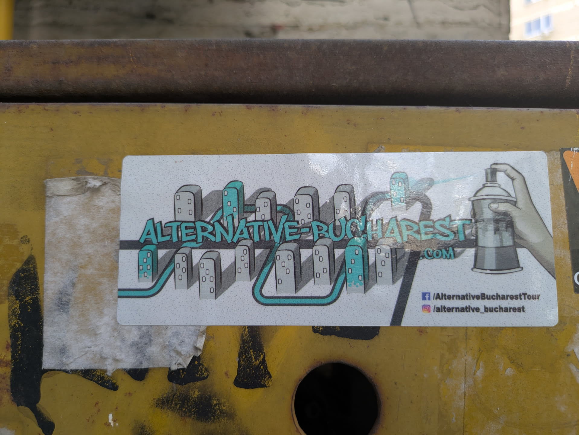 The sticker features a graphic of city buildings connected by a blue line with the words 'ALTERNATIVE-BUCHAREST .COM' and a hand spraying a can of paint. It also features social media icons for Facebook and Instagram.
