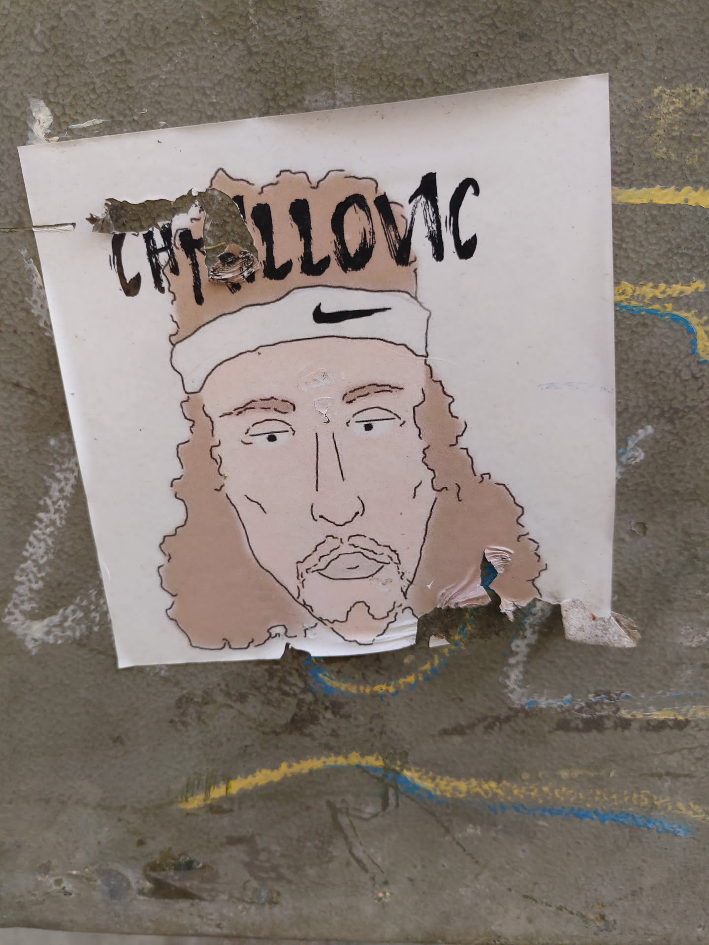 A sticker featuring a hand-drawn illustration of tennis player Casper Ruud.  The illustration shows Ruud with his characteristic long hair and a headband.  The sticker is slightly torn at the edges.