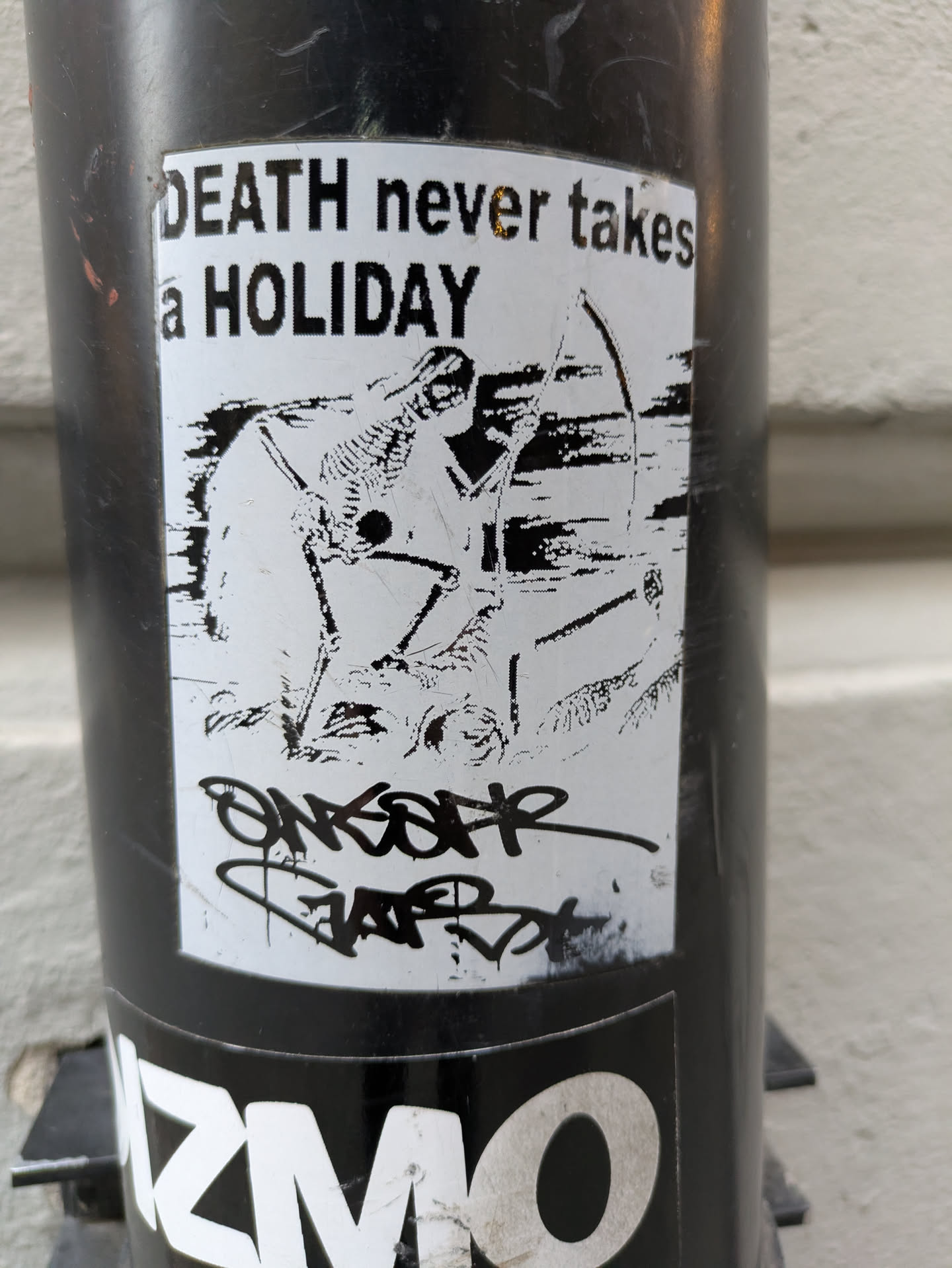 Black and white sticker with an illustration of a skeleton aiming a bow and arrow. The text 'DEATH never takes a HOLIDAY' is written at the top. There is also some graffiti-style tagging at the bottom.