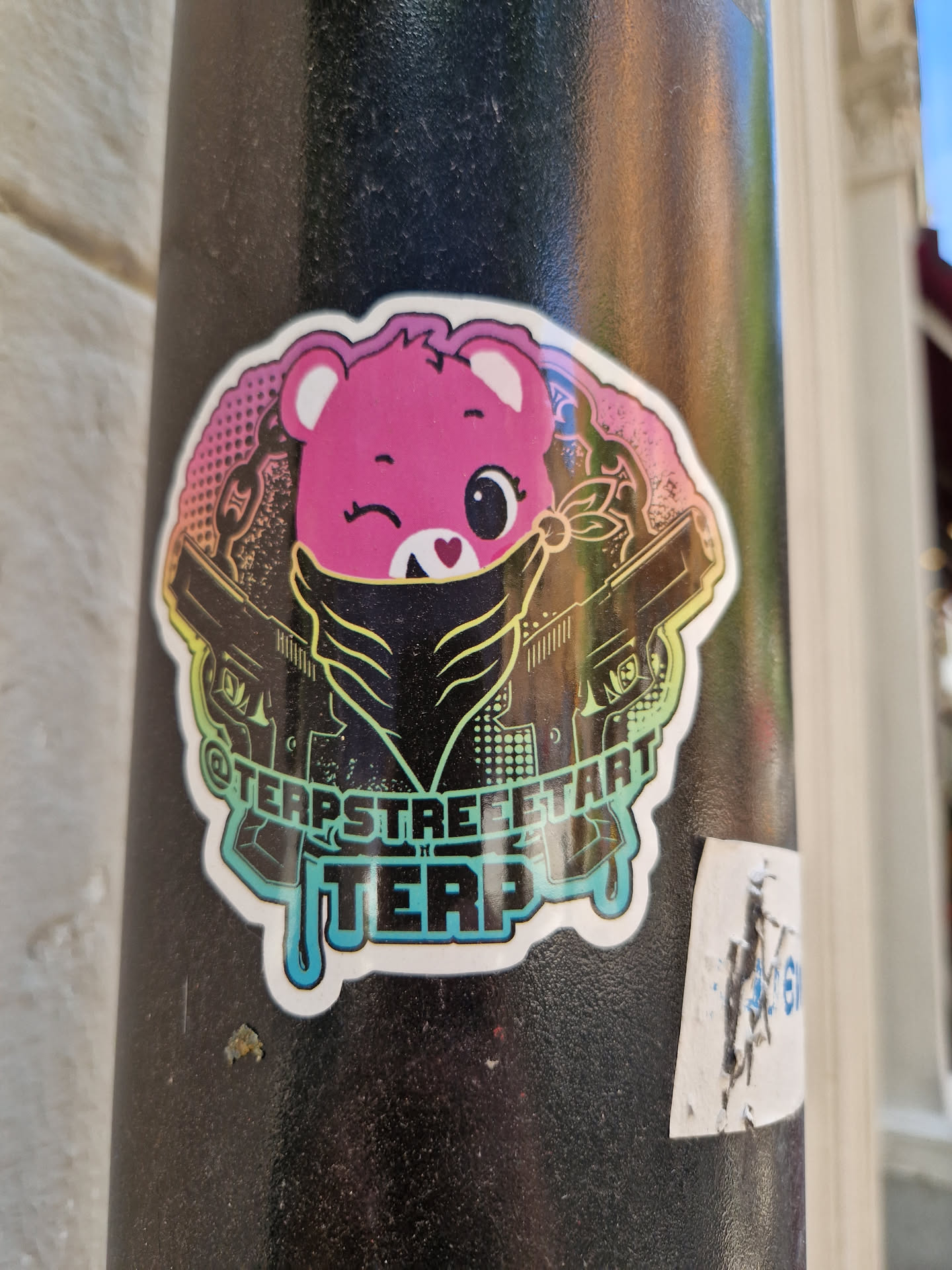 A sticker featuring a cute, pink bear wearing a bandana and wielding two guns. The style is a blend of cute and edgy. The text '@terpstreetart' and 'TERP' is visible on the sticker. 