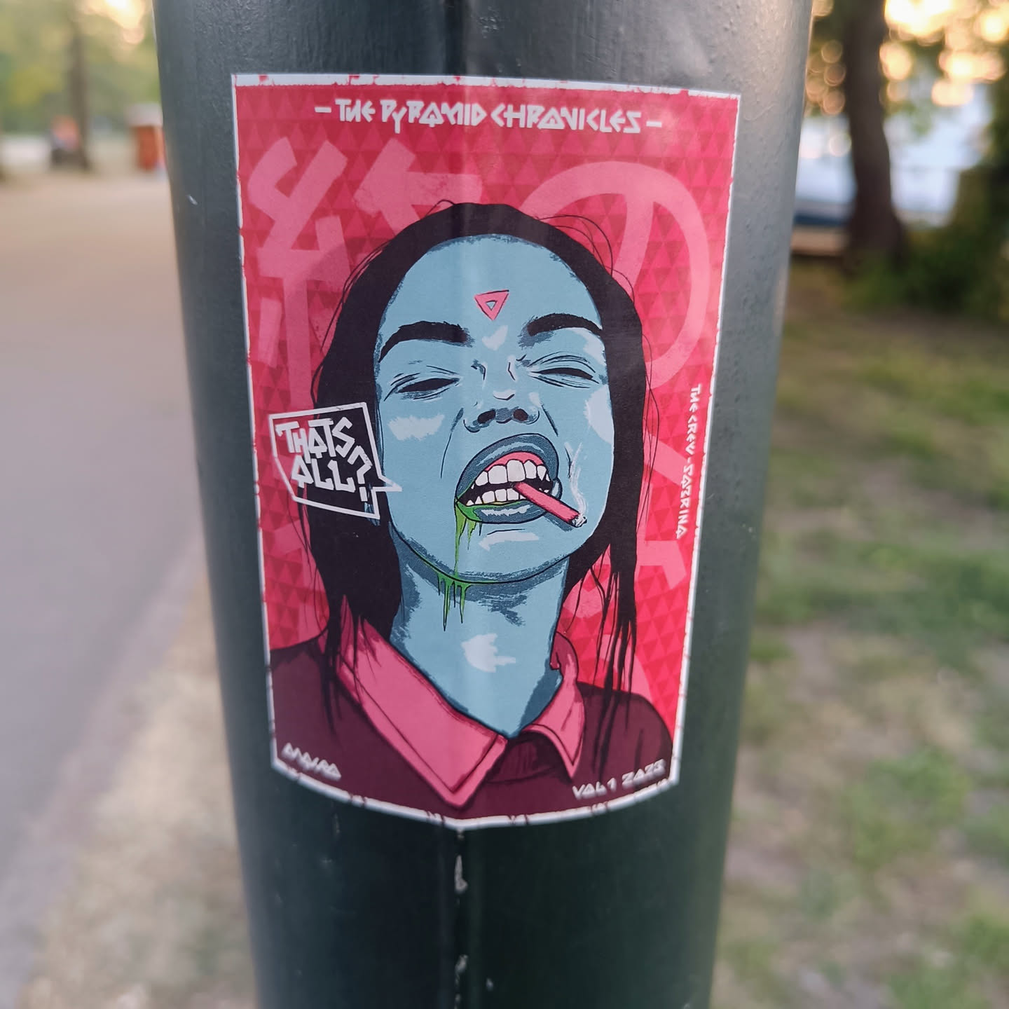 A sticker featuring a stylized illustration of a woman with a cigarette, green slime dripping from her mouth. The art style is reminiscent of psychedelic and urban art. The background is predominantly pink and red with geometrical shapes and patterns. The sticker also includes text that says "That's All?" and "The Pyramid Chronicles".