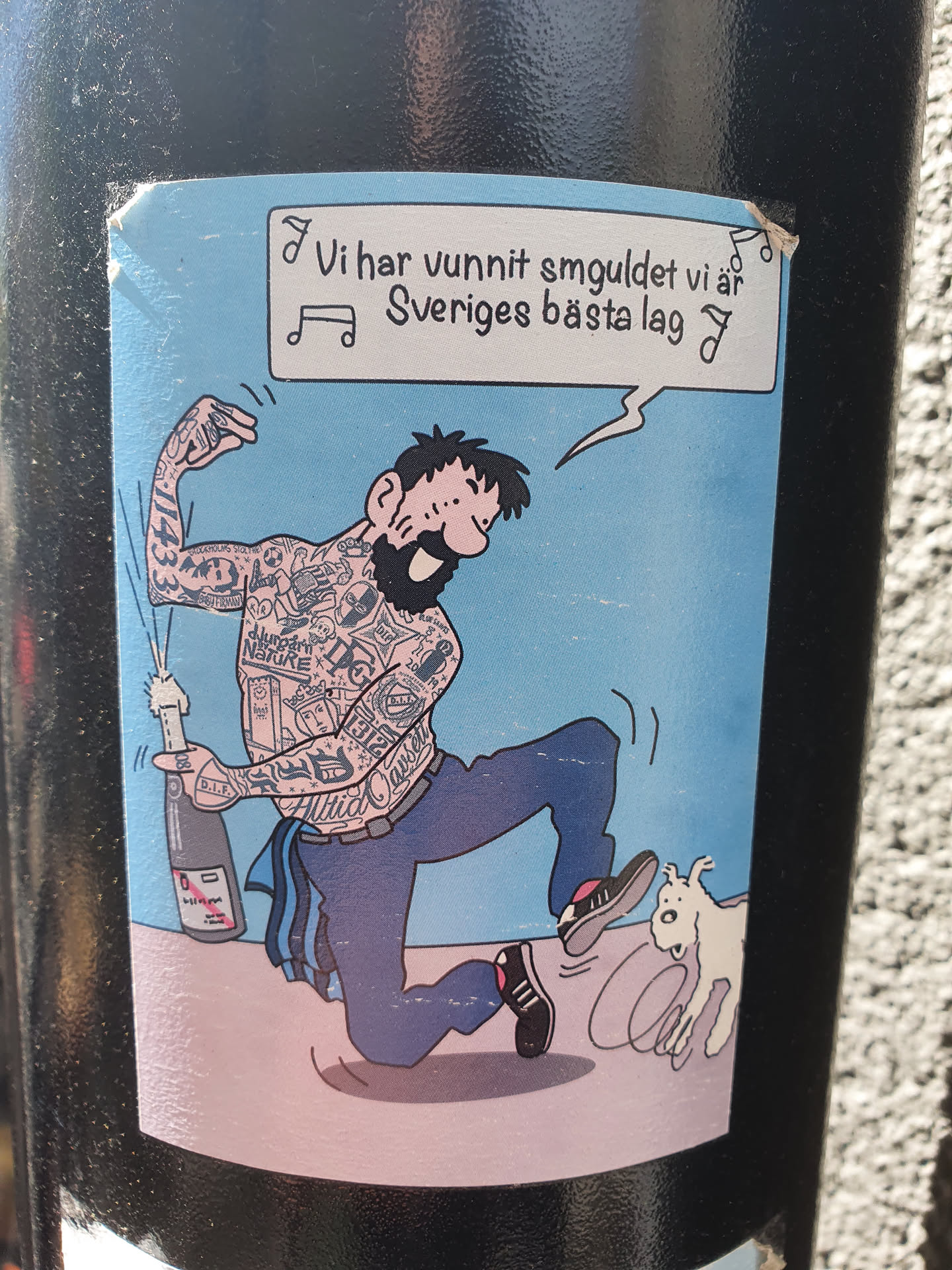 A sticker featuring a cartoon illustration of a heavily tattooed man celebrating with a bottle of champagne. A small dog is shown running away from him. The text on the sticker translates to: "We have won the gold, we are Sweden's best team."