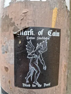 Black and white sticker with a illustration of a devil-like creature. The text on the sticker says: Mark of Cain Tattoo Stockholm and Bleed for the Devil. 