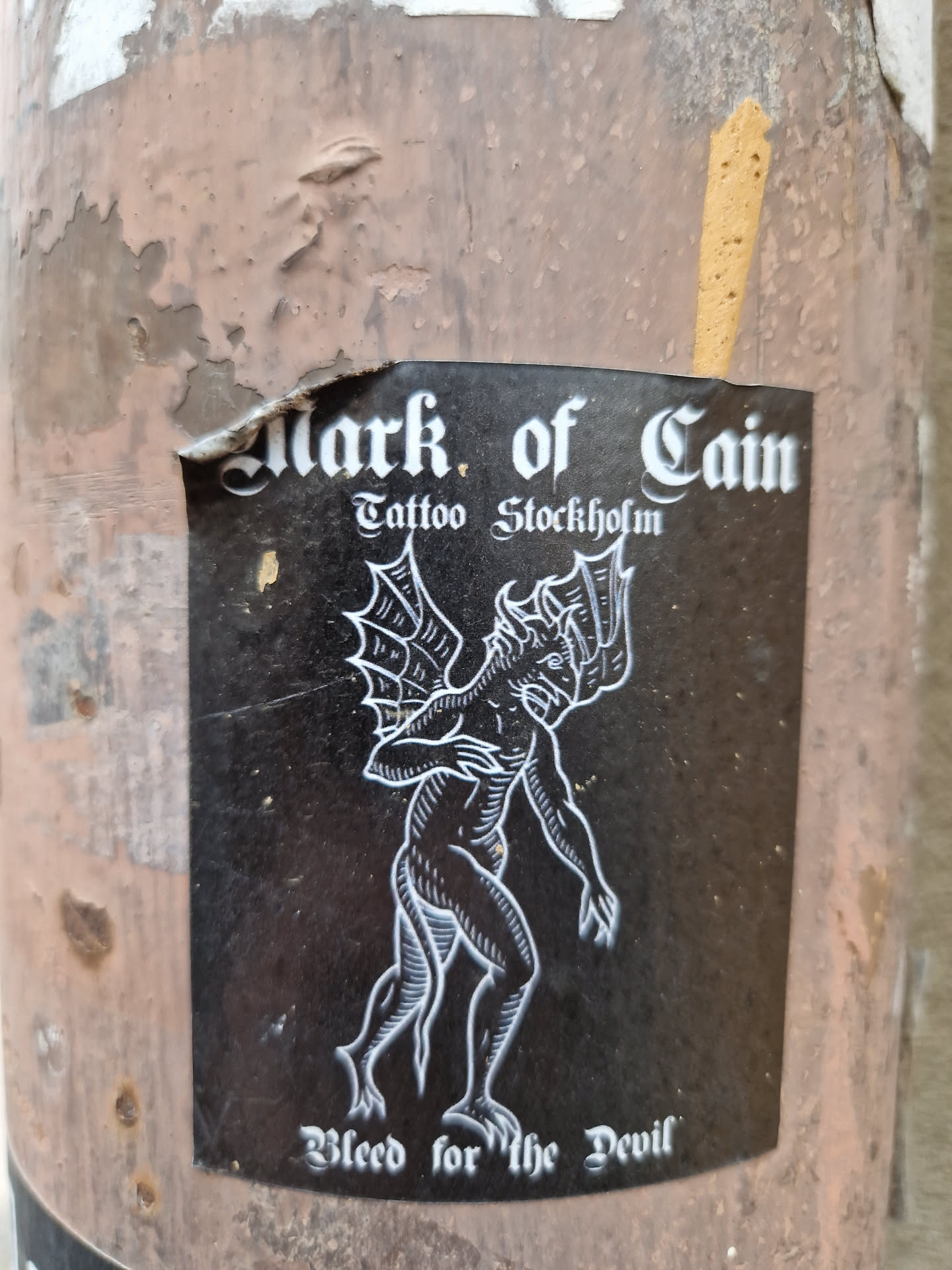 Black and white sticker with a illustration of a devil-like creature. The text on the sticker says: Mark of Cain Tattoo Stockholm and Bleed for the Devil. 