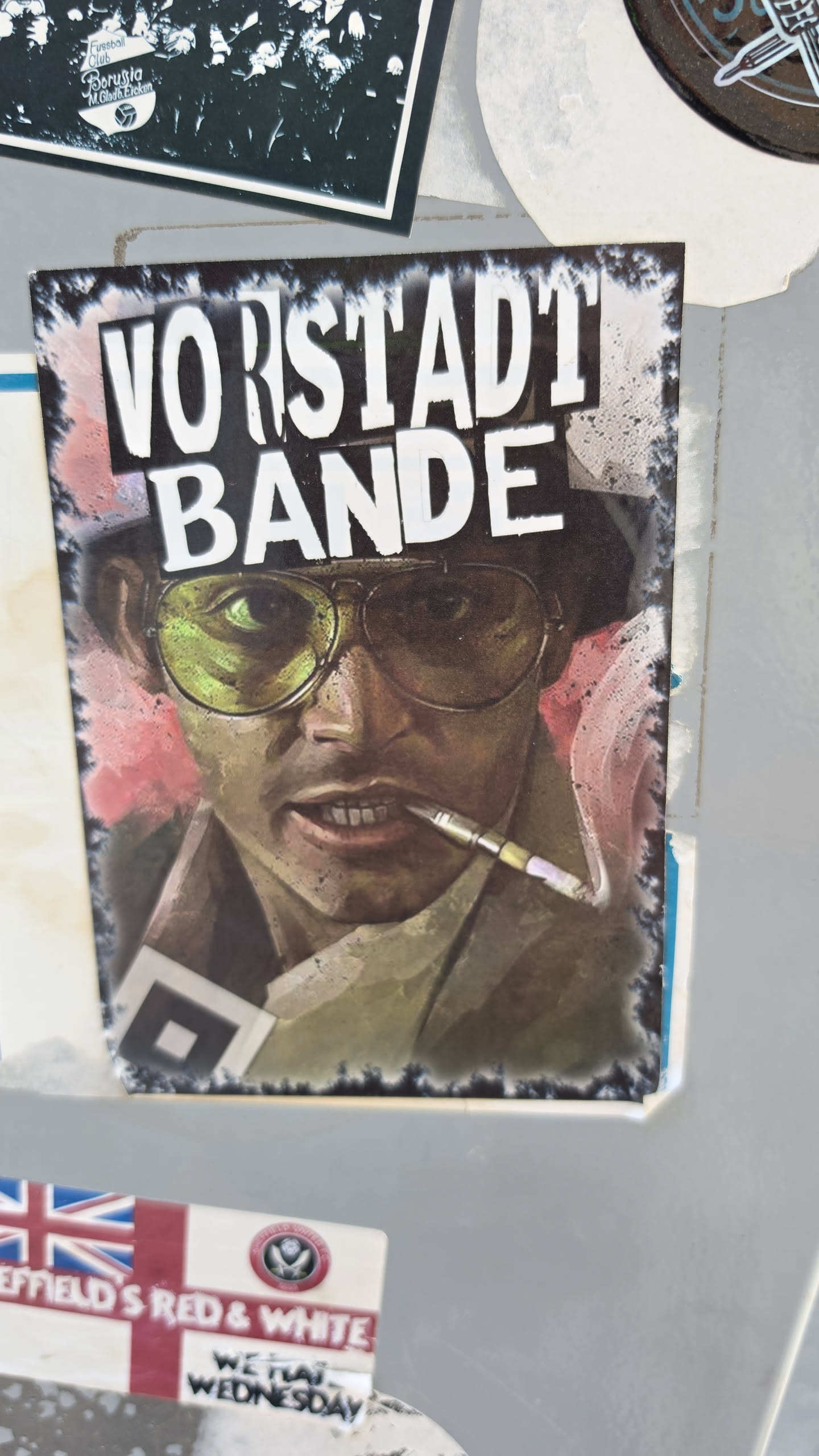 A vertical rectangular sticker depicting an artistic portrait of Raoul Duke from Fear and Loathing in Las Vegas, wearing yellow-tinted aviator glasses, a bucket hat, and holding a cigarette holder between his teeth. Above the character, the bold white text 'VORSTADT BANDE' is displayed against a dark smoky background with distressed, burned-style borders.