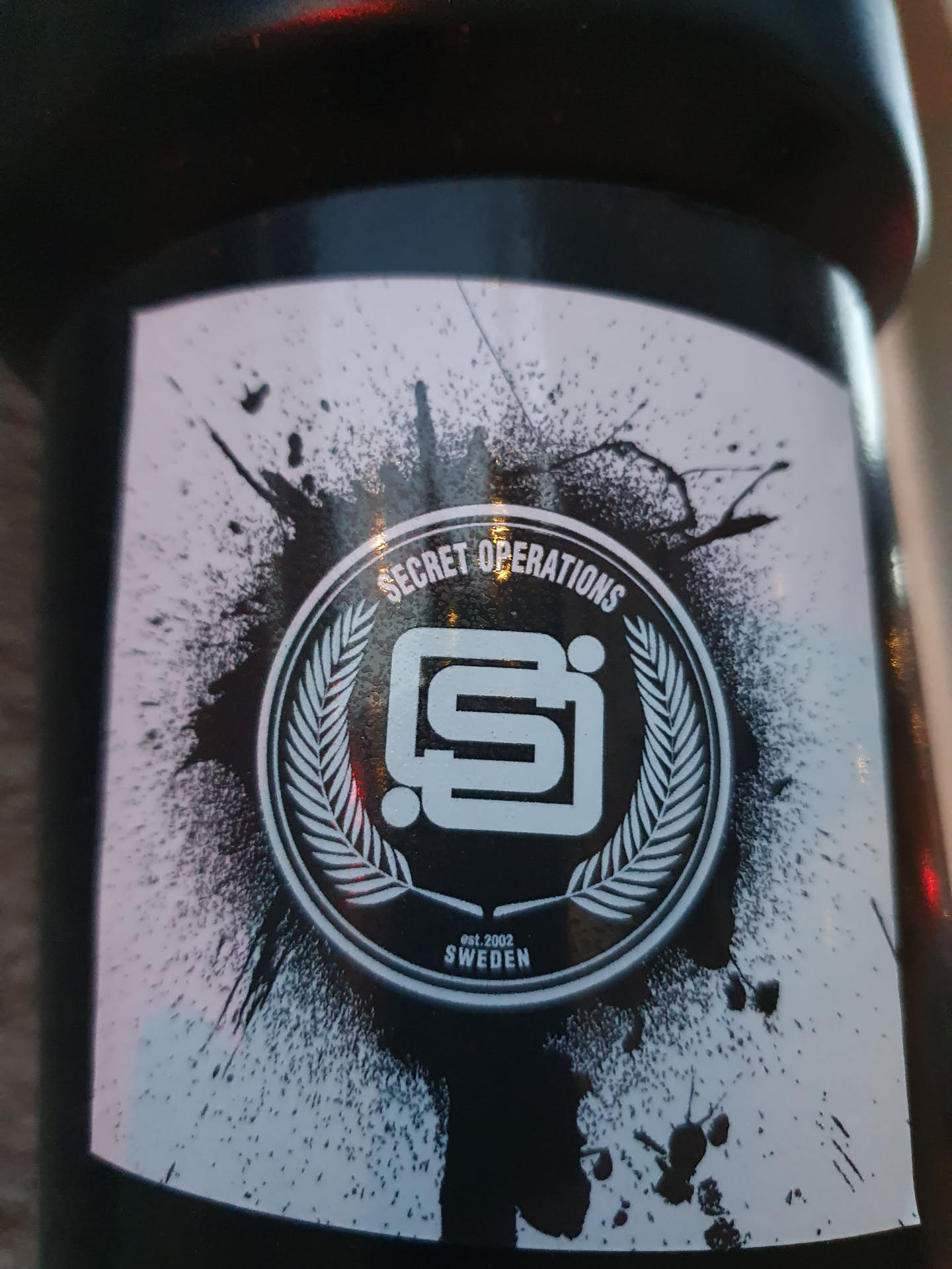 Black and white sticker with a logo featuring a stylized "SI" inside a wreath, surrounded by a paint splatter effect. The text "Secret Operations" is present above the logo, along with "Est. 2002" and "SWEDEN" below.