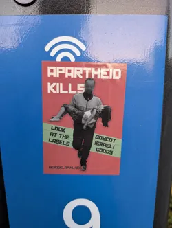 Street sticker The sticker is predominantly red with white and green text and imagery. At the top, in large white block letters, it reads 'APARTHEID KILLS'. Below this, a silhouetted figure with a blurred face carries a limp child. To the left of the figure, in green text, are the words 'LOOK AT THE LABELS'. To the right, also in green text, it says 'BOYCOT ISRAELI GOODS'. At the very bottom, in smaller white text, is 'DERODELAP.NL/BDS'. The overall design is impactful and conveys a strong political message.