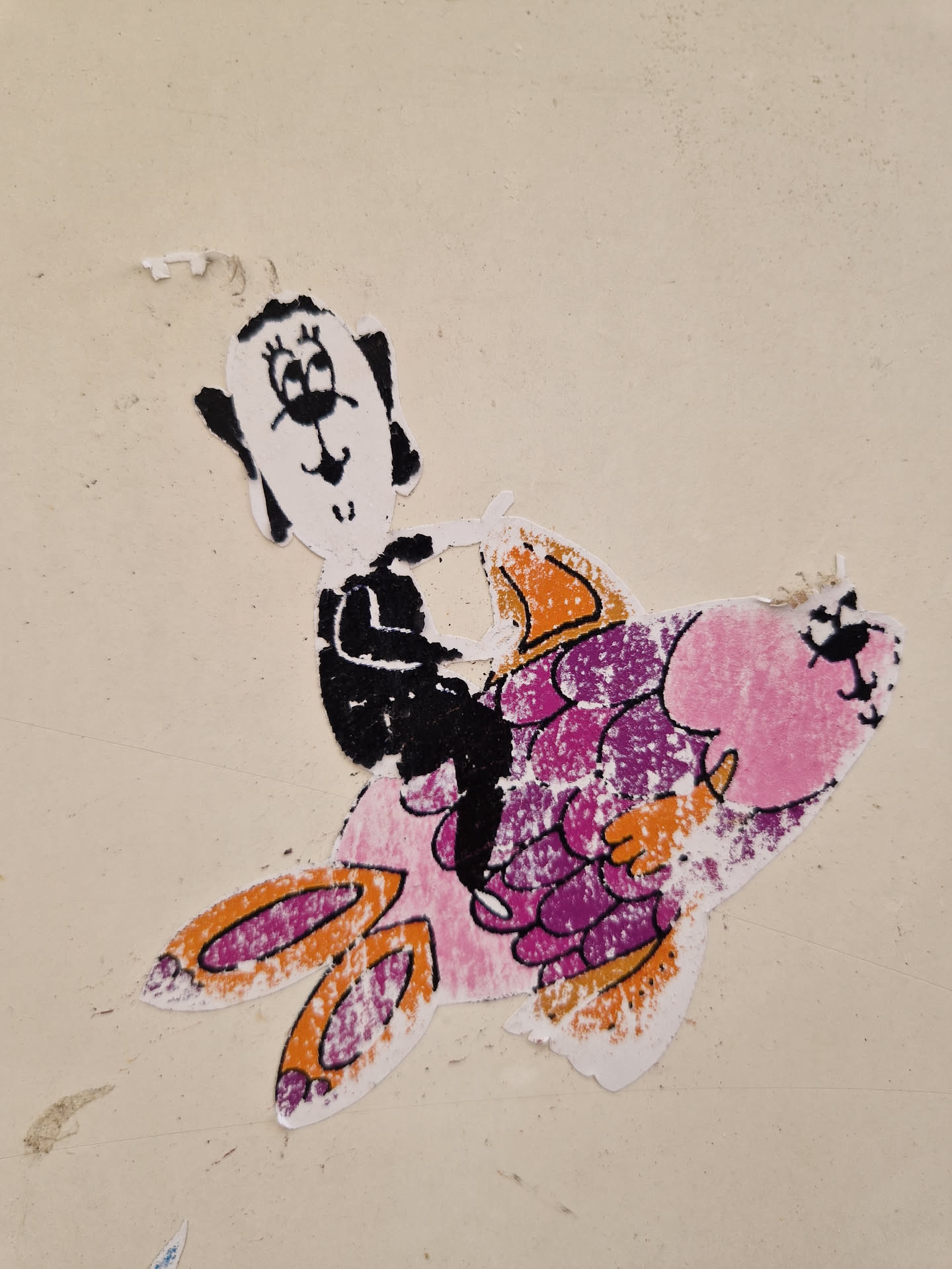 This sticker shows a simple line drawing of a dog sitting on a larger, colorful fish.  The style is childlike and playful. The sticker appears to be slightly worn or weathered.