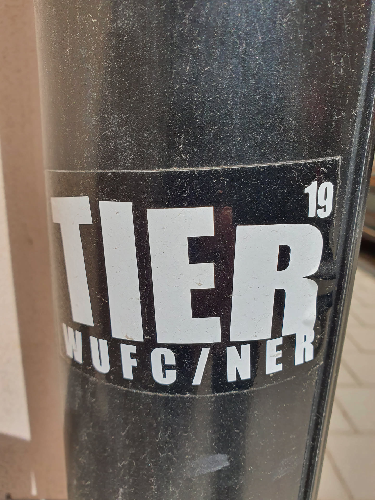 A black and white sticker with the word TIER in large white capital letters. Below it, in smaller letters, it says WUFC/NER. In the top right corner, the number 19 is visible.